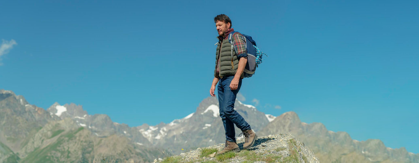 Alex Hugo (Samuel Le Bihan) debout sur une montagne, derrière lui une montagne