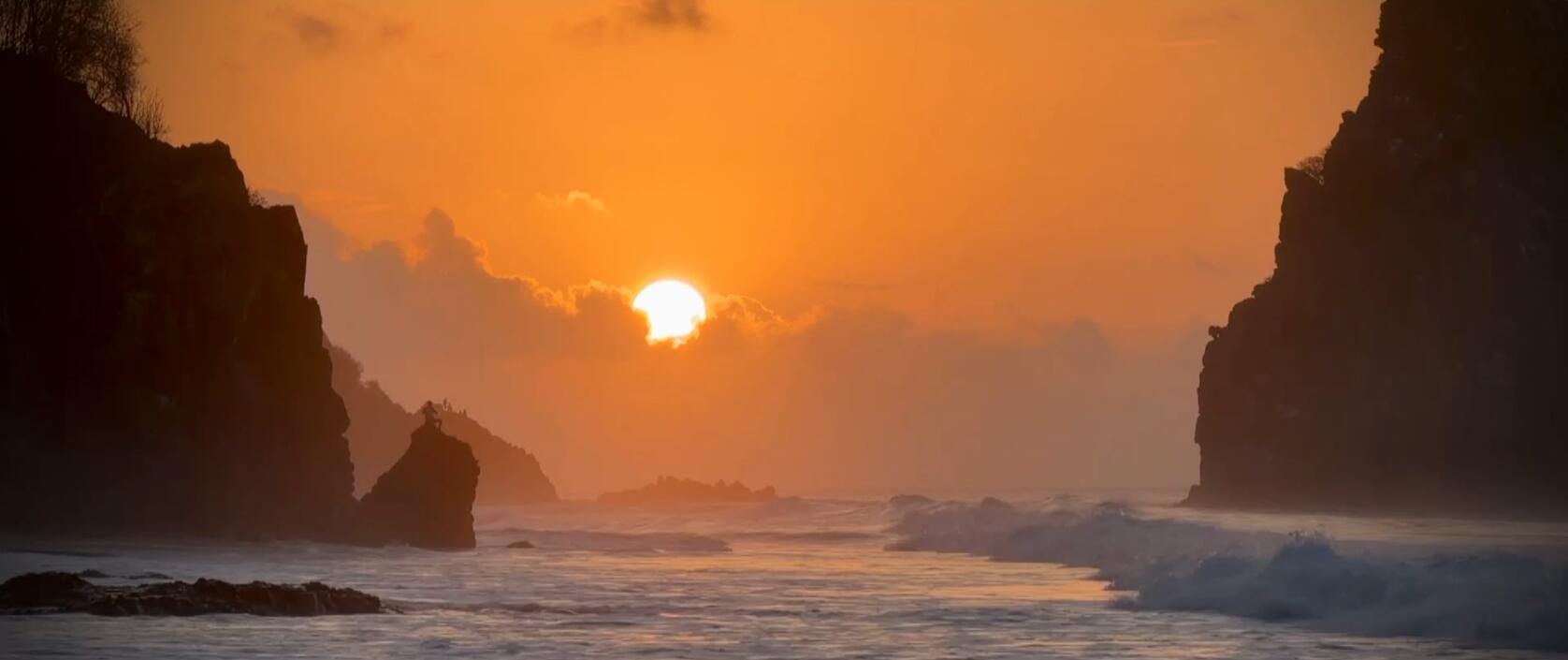 Photo. Vue d'un couché de soleil orangé en pleine mer. Sur les cotés gauche et droite des falaises